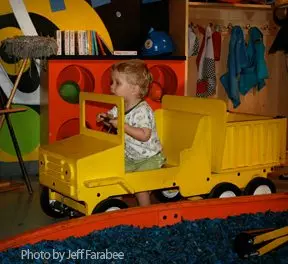 Child riding in foot-powered, yellow truck.
