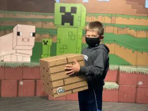 Photo of a kid holding minecraft inspired block in front of a stack of more blocks
