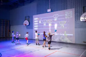 Children playing with a giant, projected, interactive screen on a wall using gym balls