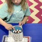 Child practices counting by putting marshmallows over an illustration of hot chocolate
